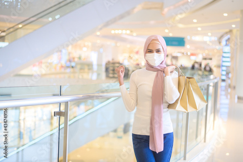 Young muslim woman wearing protective mask in shopping mall, shopping under Covid-19 pandemic concept.