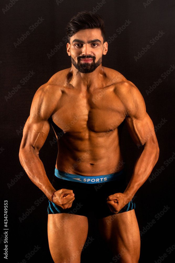 Muscular bodybuilder male in gym. Black background. Front profile. Looking at camera. Showing chest and shoulder muscles Muscular bodybuilder male in gym. Black background. Front profile. Looking at camera. Showing chest and shoulder muscles