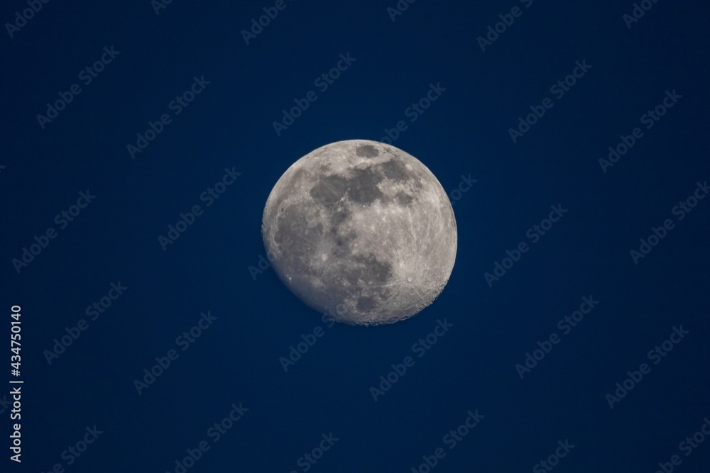 A portrait of the moon in a dark blue sky. The moon is in between a full and a half moon and is centered in the frame. A portrait of the moon in a dark blue sky. The moon is in between a full and a half moon and is centered in the frame.