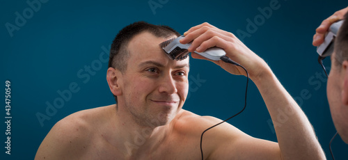 Mature man is cutting his hair by electric hair clipper in front of the mirror.