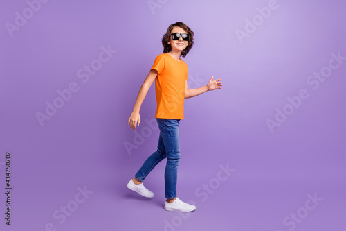 Full length body size view of attractive cheerful boy walking isolated over violet purple color background