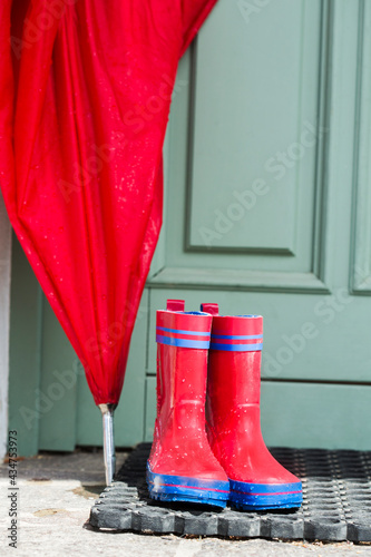 rote Gummistiefel und Schirm vor Eingangstür, Regentag