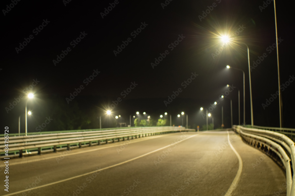 An empty country road with bumpers, lit by street lights. Blurred focus
