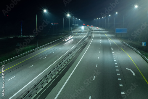 High-speed suburban highway in the light of streetlights. There is a white marking arrow on the asphalt