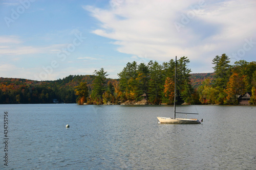 Sailboat on calm lake with fall foliage and quaint cabins