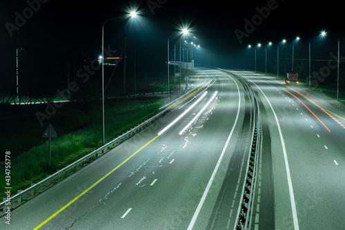 An expressway with long red and white light strips from the headlights of cars, in the light of streetlights. A truck is parked on the side of the road