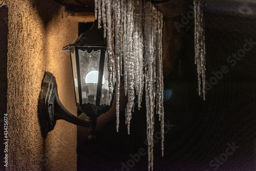 icicles hanging from the roof by a lighted lamp
