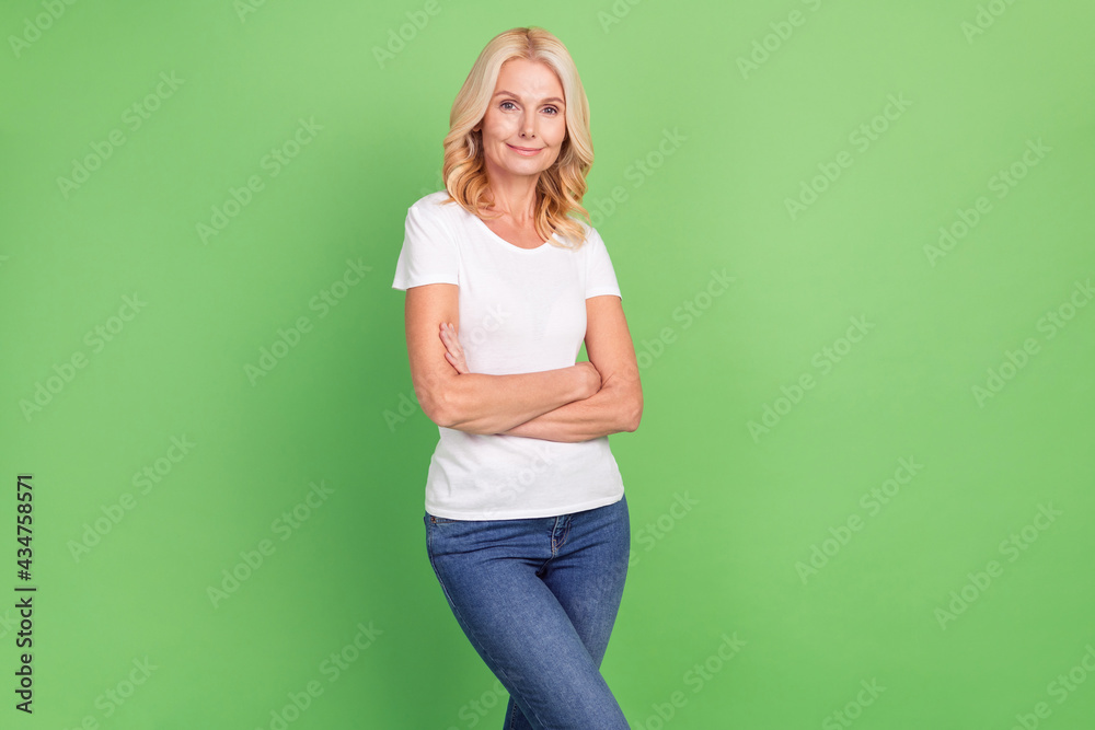 Photo portrait senior woman confident smiling with crossed hands wearing t-shirt jeans solated pastel green color background Photo portrait senior woman confident smiling with crossed hands wearing t-shirt jeans solated pastel green color background