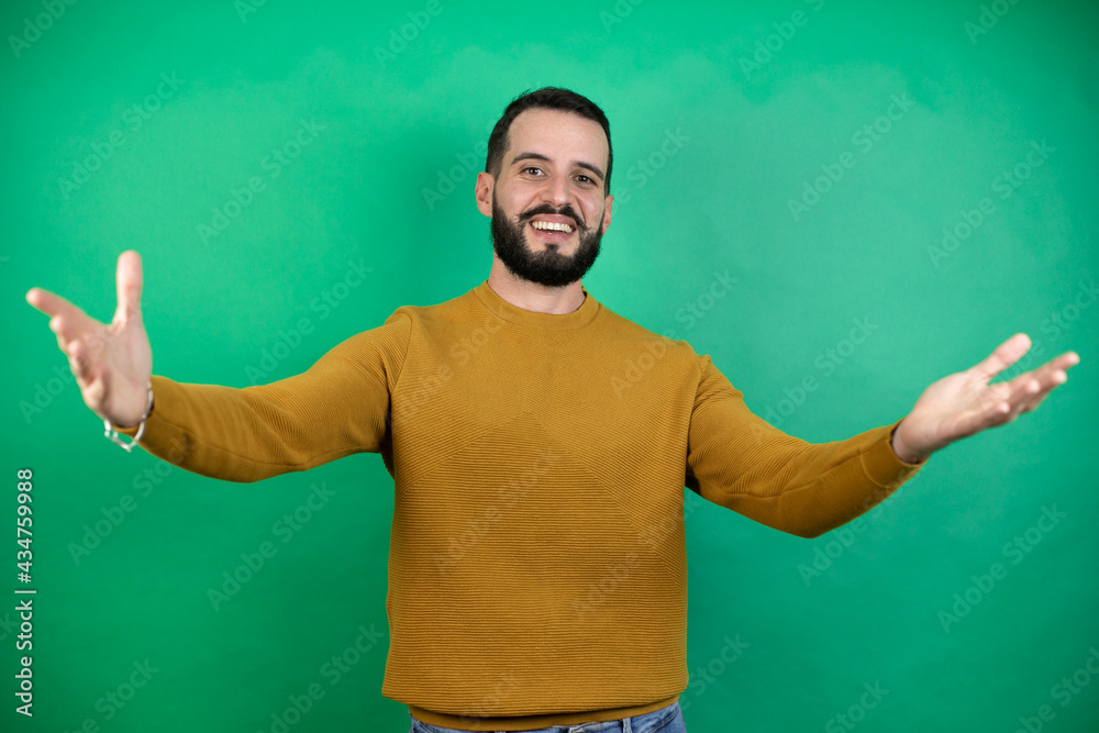 Handsome man wearing casual clothes over isolated green background looking at the camera smiling with open arms for hug