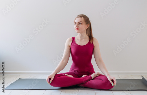Young healthy beautiful woman practicing yoga at home sitting in lotus pose on yoga mat meditating relaxed. Indoor and outdoor workout. Sport and healthy active lifestyle concept.