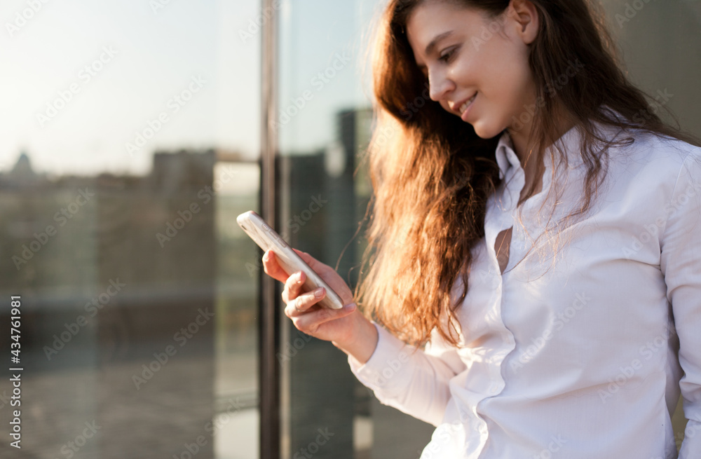Fototapeta premium Young woman holding a mobile phone and smiling, texting or using social media