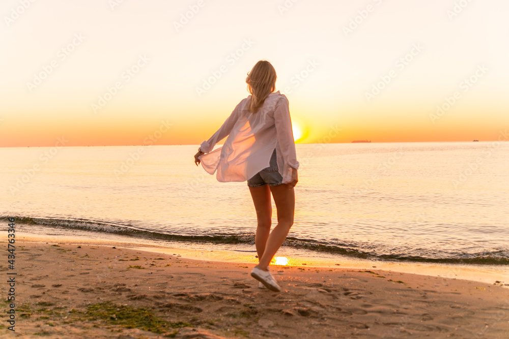 A slender girl in white clothes runs along the beach against the background of the sea. A sports girl runs along the embankment of the sea. Healthy woman on the beach