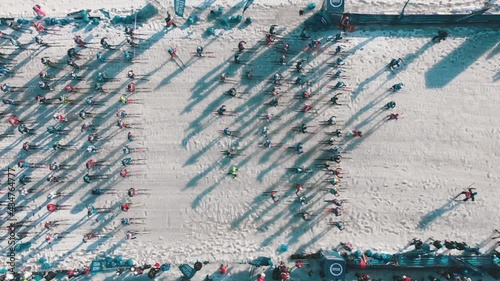 Ski athletes prepare for race competition start lining up casting shadows on snowy trail at winter morning sunlight aerial view