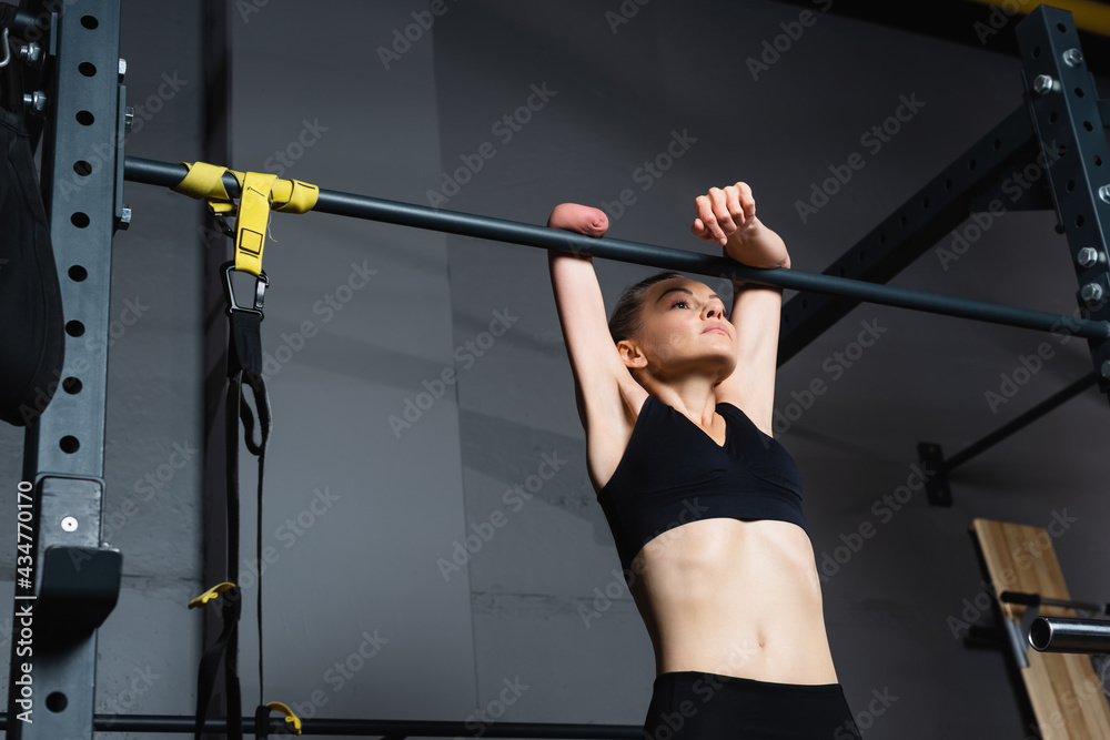 Fototapeta premium strong-willed amputee woman working out on horizontal bar in gym