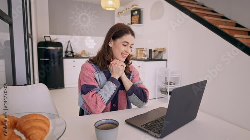 young woman has video call with friend friendship online sitting at the table in the kitchen photo