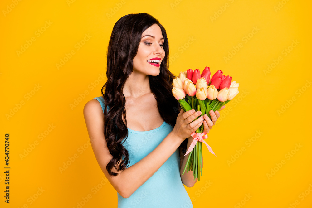 Photo of positive lady hold bouquet tulips tender face wear blue singlet isolated yellow color background Photo of positive lady hold bouquet tulips tender face wear blue singlet isolated yellow color background