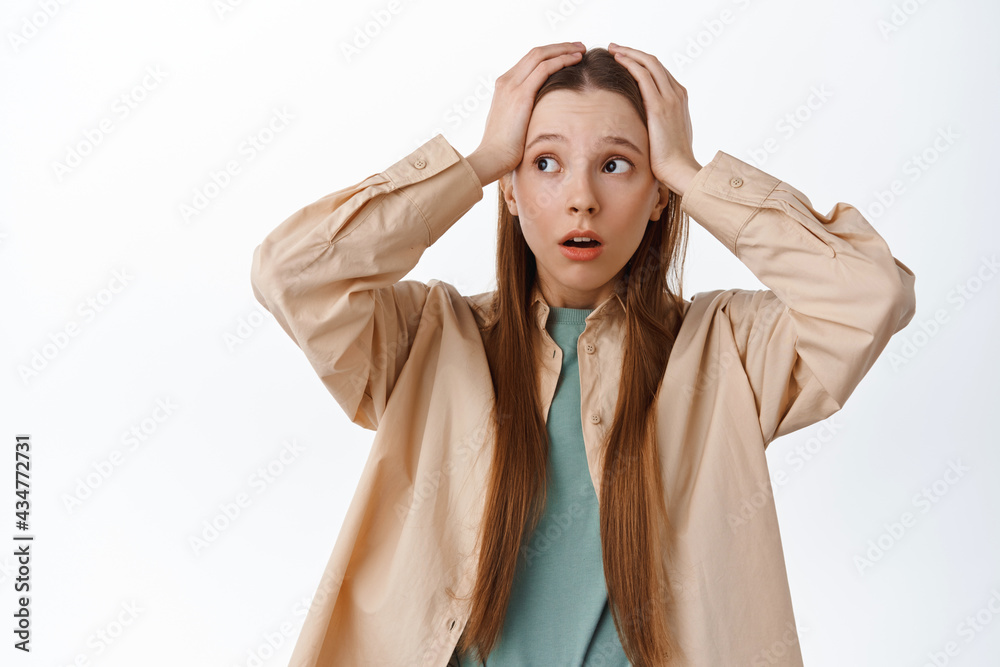 Anxious young woman holding hands on head, panicking and looking aside at logo, having proble, standing troubled and worried against white background Anxious young woman holding hands on head, panicking and looking aside at logo, having proble, standing troubled and worried against white background
