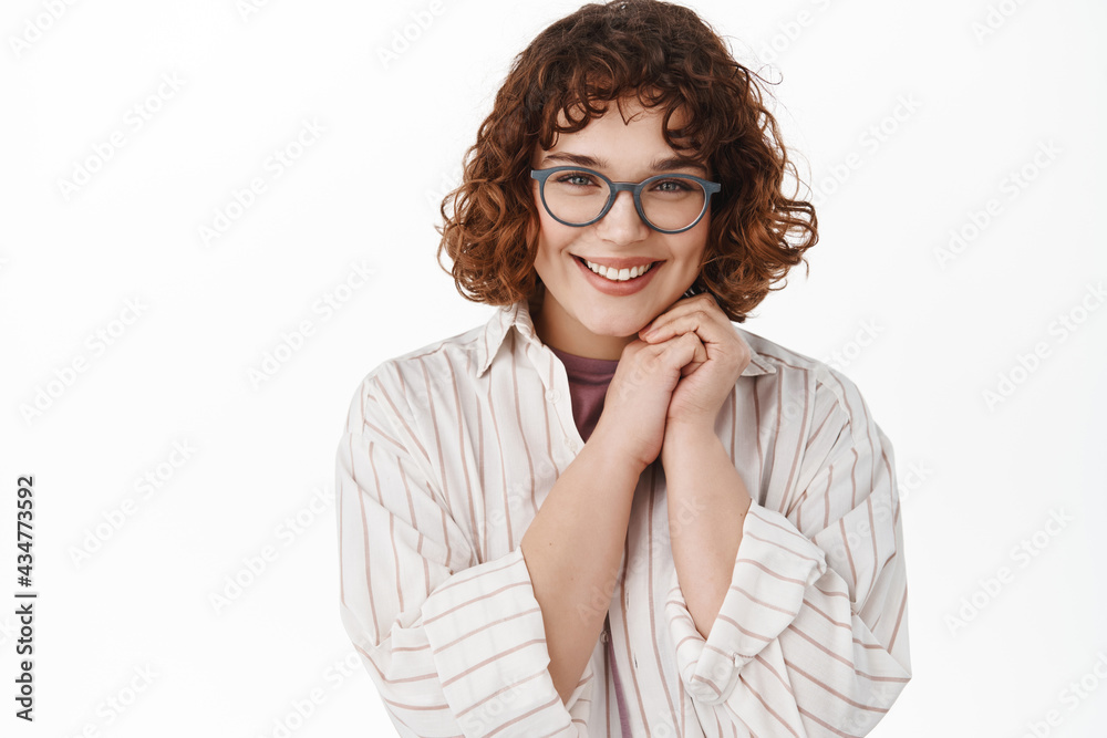 Obraz premium Close up of beautiful young woman in glasses looking coy and tender at camera, blushing, flirting or looking at something nice, standing romantic against white background