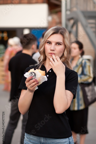 Pretty young blonde woman eating hamburger outdoor on the street