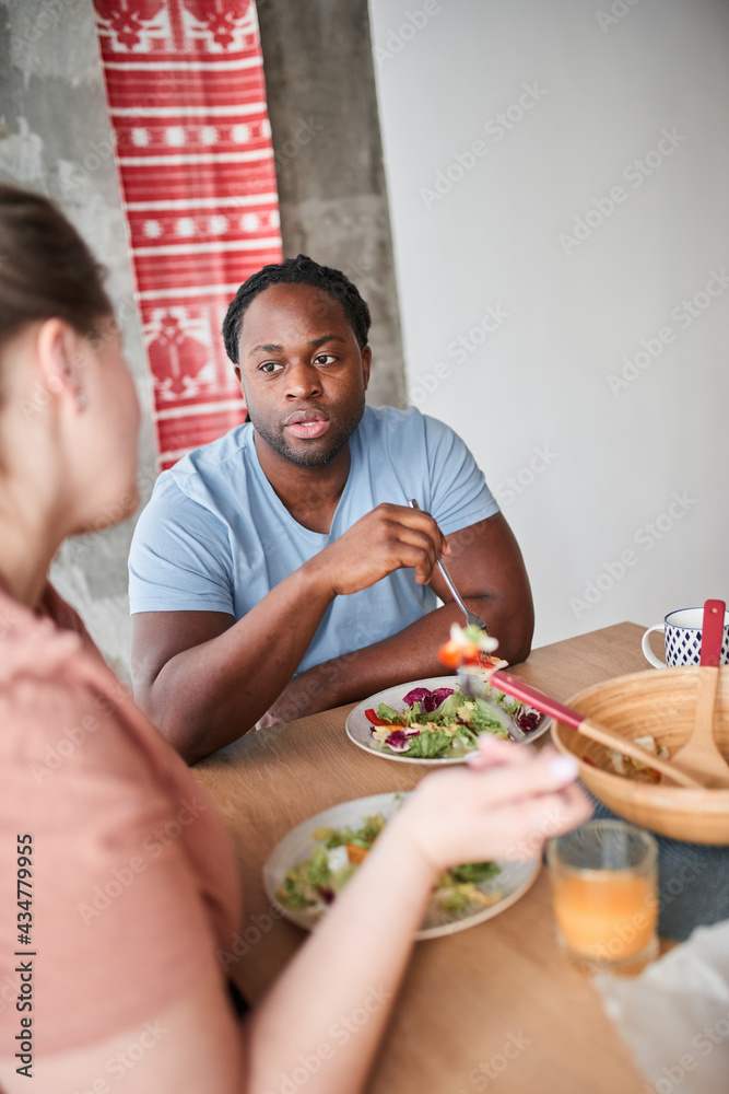 Man holding fork and looking at his wife while eating salad