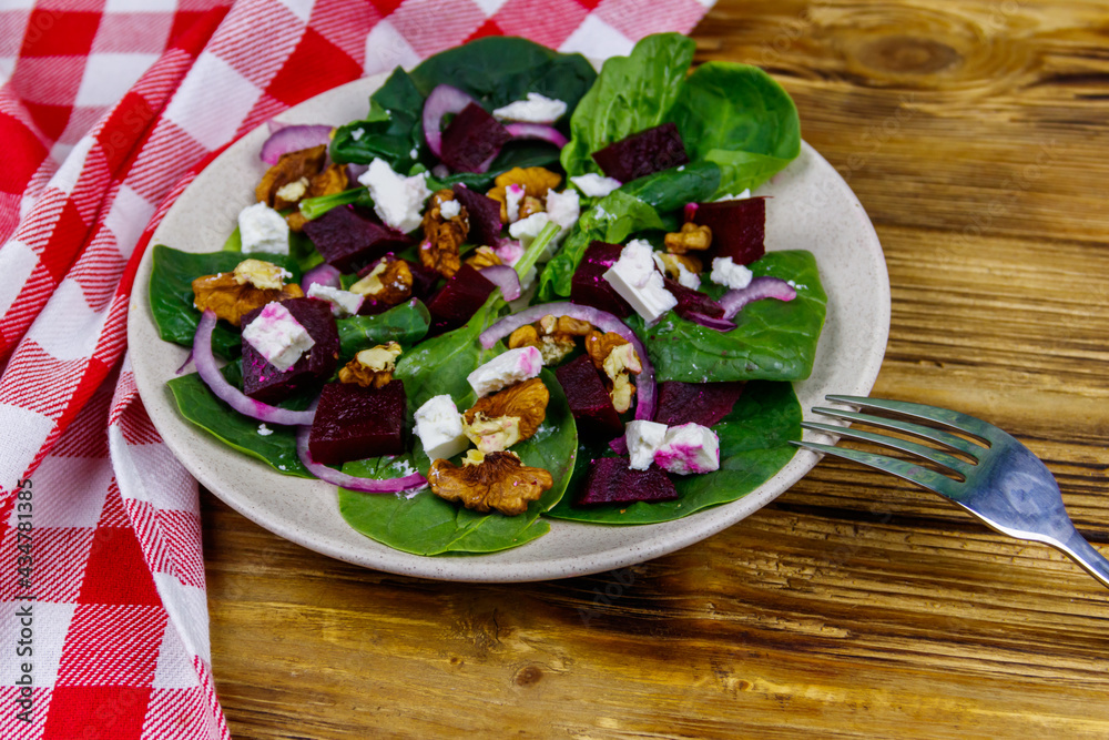 Tasty spinach salad with boiled beetroot, feta cheese, walnut and red onion on wooden table. Healthy vegetarian food Tasty spinach salad with boiled beetroot, feta cheese, walnut and red onion on wooden table. Healthy vegetarian food