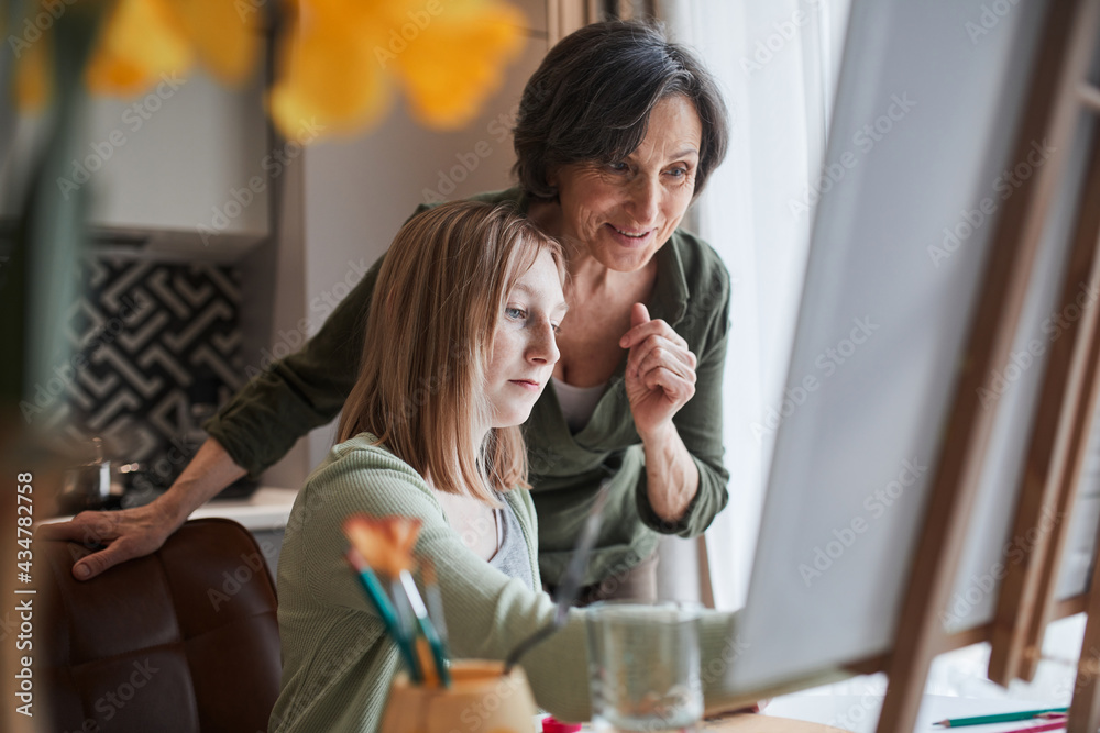 Woman looking with satisfaction at the drawing of her blonde granddaughter Woman looking with satisfaction at the drawing of her blonde granddaughter