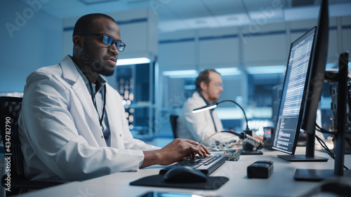 Modern Electronics Development Facility: Black Engineer and Diverse Team of Multi-Ethnic Scientists Work on Computers, use CAD Software, Design Industrial PCB, Silicon Micro Chips, Semiconductors