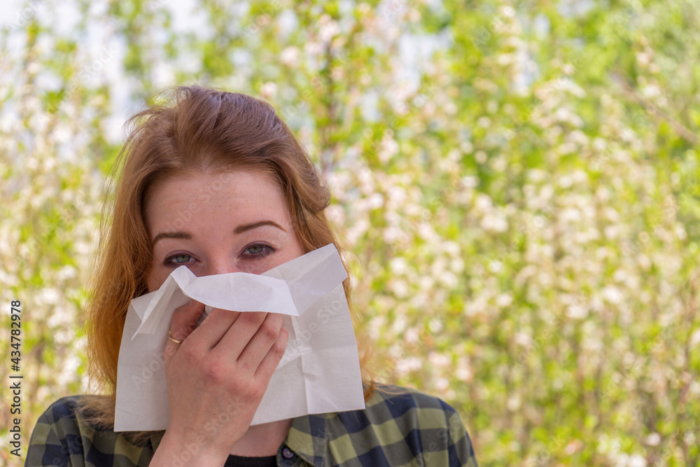 Season allergy to flowering plants pollen. Young woman with paper handkerchief in hand covering her nose in garden. Teen girl sneezing against blossoming trees. Seasonal allergy prevention Season allergy to flowering plants pollen. Young woman with paper handkerchief in hand covering her nose in garden. Teen girl sneezing against blossoming trees. Seasonal allergy prevention