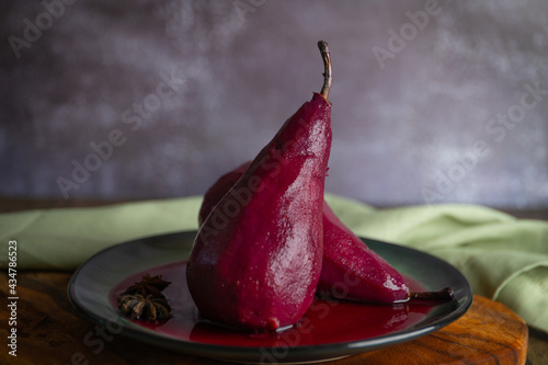 Two pears in red wine on a ceramic plate and concrete wall background.