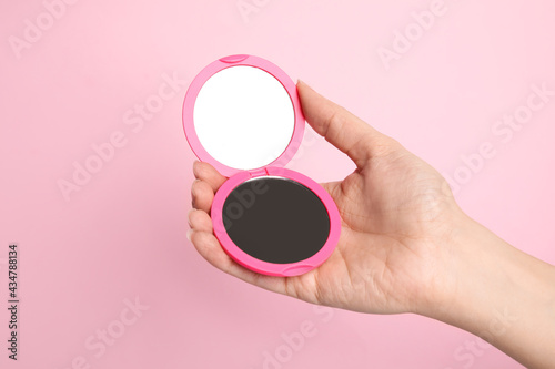 Woman holding stylish cosmetic pocket mirror on pink background, closeup photo