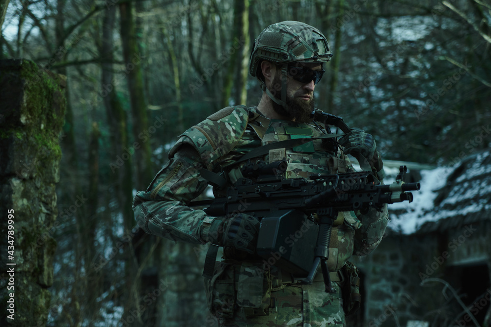 Fototapeta premium Portrait of airsoft player in professional equipment with machine gun in the forest. Soldier with weapons at war