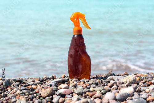 Oil spay sunscreen, sunblock or tanning lotion advertisement idea. Clear brown bottle standing at the seaside on a sunny day. Summertime fresh inspirational wallpaper