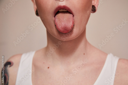 Extravagant woman with piercing at her face showing her tongue while posing