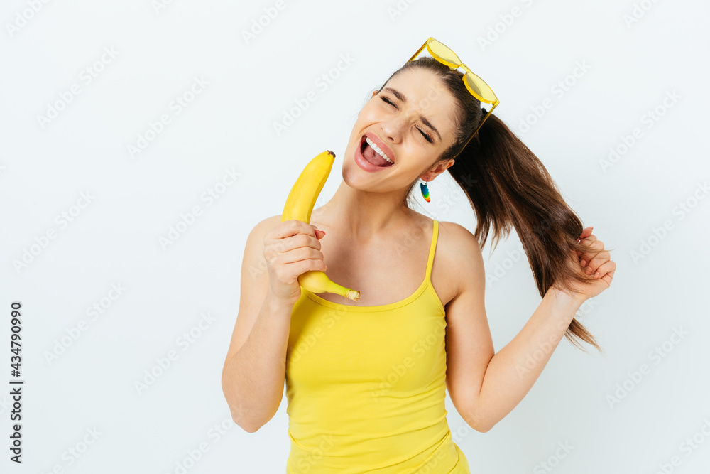 Joyful young woman singing using banana as microphone Joyful young woman singing using banana as microphone