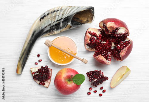 Honey, pomegranate, apples and shofar on white wooden table, flat lay. Rosh Hashana holiday photo