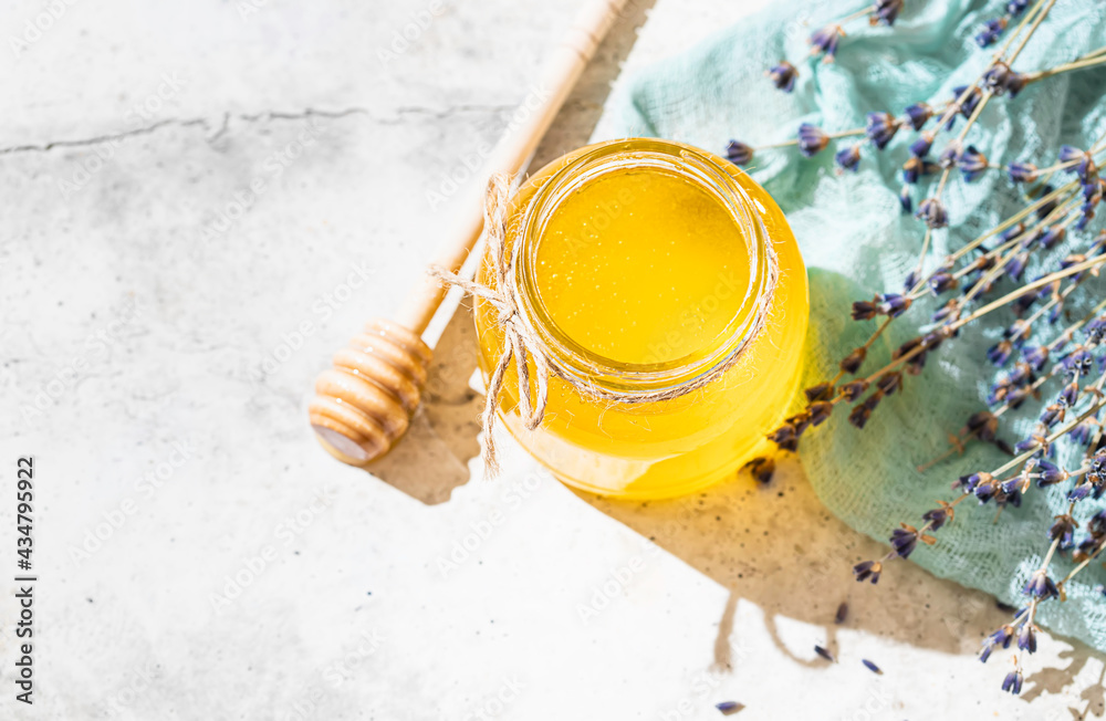 Fototapeta premium Flowing honey from wooden dipper in a glass jar. Organic honey dipping from the wooden honey spoon. Lavender honey
