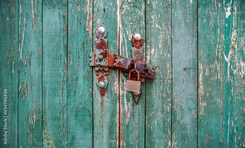 Old wooden gate with a rusty barn lock on a green background Old wooden gate with a rusty barn lock on a green background