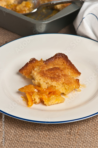 top view, close distance of a square of apricot Buckle, dessert, on a round, white plate with a blue rim 