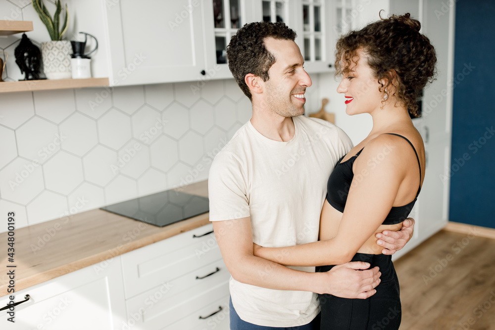 Happy young couple stand in modern kitchen at home hugging enjoy morning together. Smiling millennial man and woman celebrate relocation moving to new apartment. Happy young couple stand in modern kitchen at home hugging enjoy morning together. Smiling millennial man and woman celebrate relocation moving to new apartment.