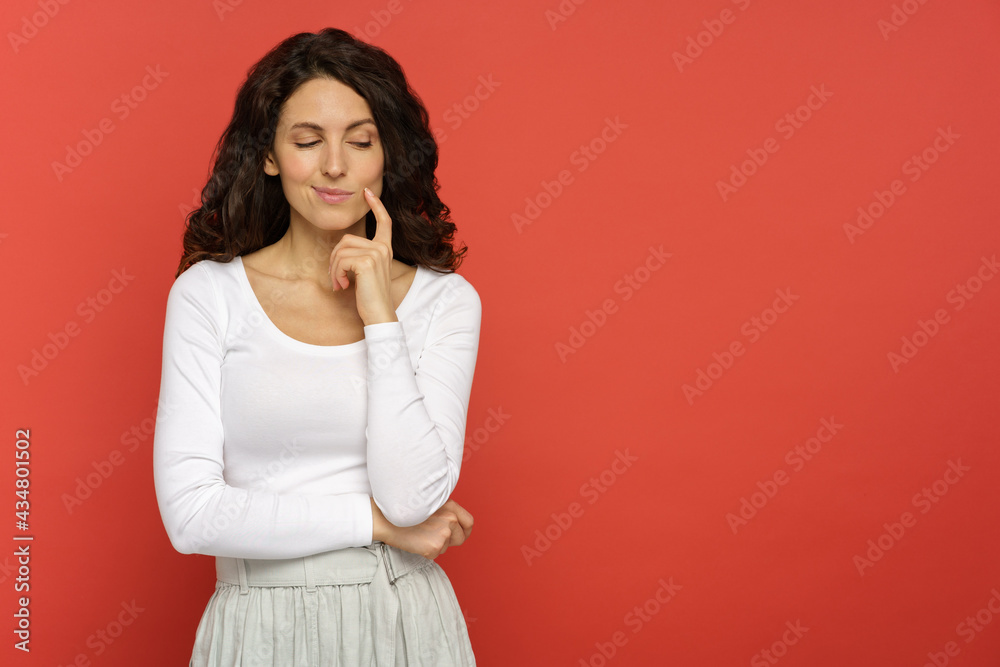 Portrait of curly young female look down with cunning smile think on new idea, plan, strategy, action over red background with copy space. Tricky millennial woman thoughtful ponder with finger on chin Portrait of curly young female look down with cunning smile think on new idea, plan, strategy, action over red background with copy space. Tricky millennial woman thoughtful ponder with finger on chin