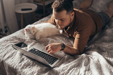 Man laying at the stomach at the bed and using touchpad of his laptop