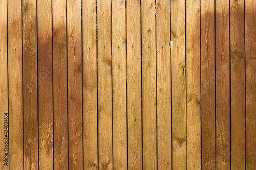 A fence made of wood planks treated with an antiseptic. There are two large patches of dark brown paint and small debris from paper notices. Background. Texture.