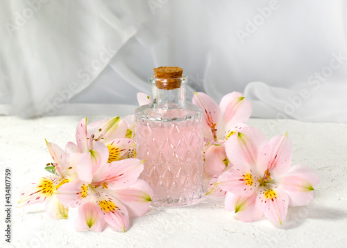 Perfume or aromatic oil glass with flowers over light background. Close up composition for spa, aromatherapy or massage. Relaxation. Wellness. Natural organic cosmetics.