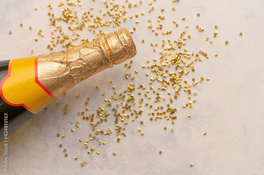 Obraz premium The photo shows a fragment of a bottle of champagne in a bright gold wrapper. Nearby is confetti. White background. Spirit of Christmas. Holiday spirit. White background. Place for your insert.