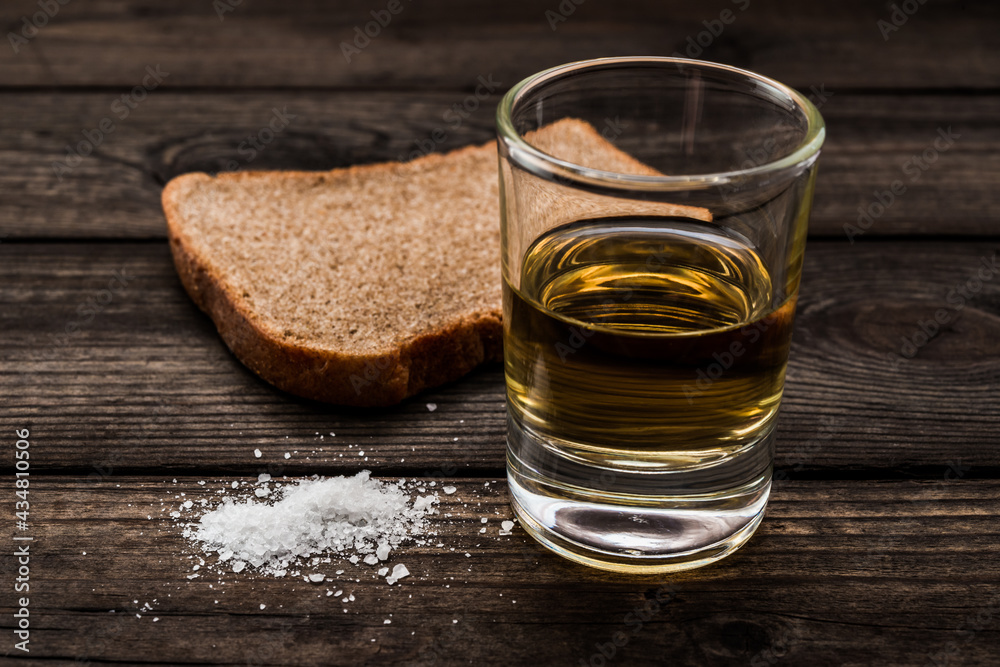 Glass of tequila with salt and piece of black bread on an old wooden table. Close up view Glass of tequila with salt and piece of black bread on an old wooden table. Close up view