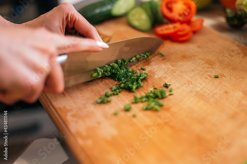 Close up shot woman standing kitchen chopping green salad dill plant products fruits and vegetables wooden cutting board. Lady preparing breakfast lunch after training, cook healthy food, copyspace. 