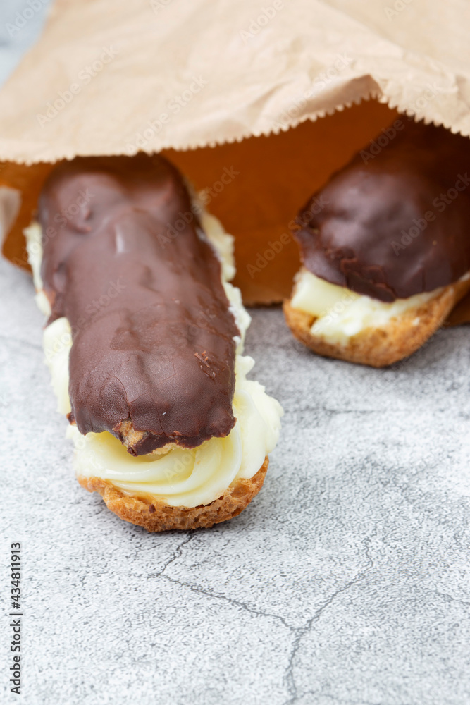 Chocolate eclair with a custard cream filling in a brown paper bag. Environmentally friendly packaging for recycling
