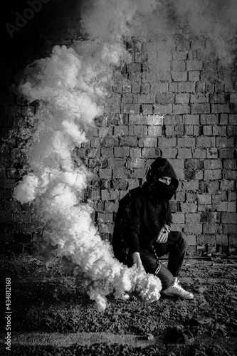 Young handsome criminal model man in a black hoodie with orange fire. Orange smoke bonfire. Hot and explosion, burning gas, danger, and inferno. Black mask, protest of the person © EvgeniaSevryukova