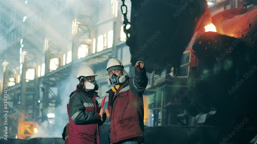Industrial workers in safety wear are talking at the metallurgical plant. Metallurgical factory equipment, metallurgy industry concept.
