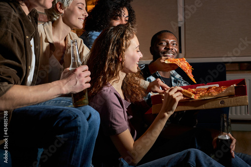 Group of friends eating pizza and watching tv.Home party.Fast food concept. Americans spending free time together in the evening. side view
